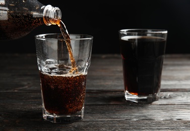Photo of Pouring refreshing soda drink into glass on black wooden table against dark background