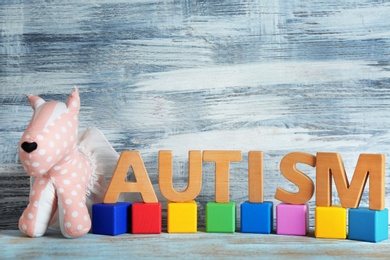 Photo of Word "Autism", toy and wooden cubes on table