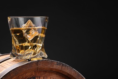 Whiskey with ice cube in glass on wooden barrel against blue background, space for text