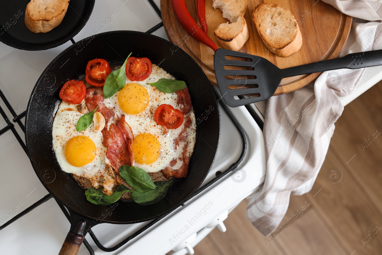 Photo of Delicious fried eggs with bacon and tomatoes in pan on stove, top view