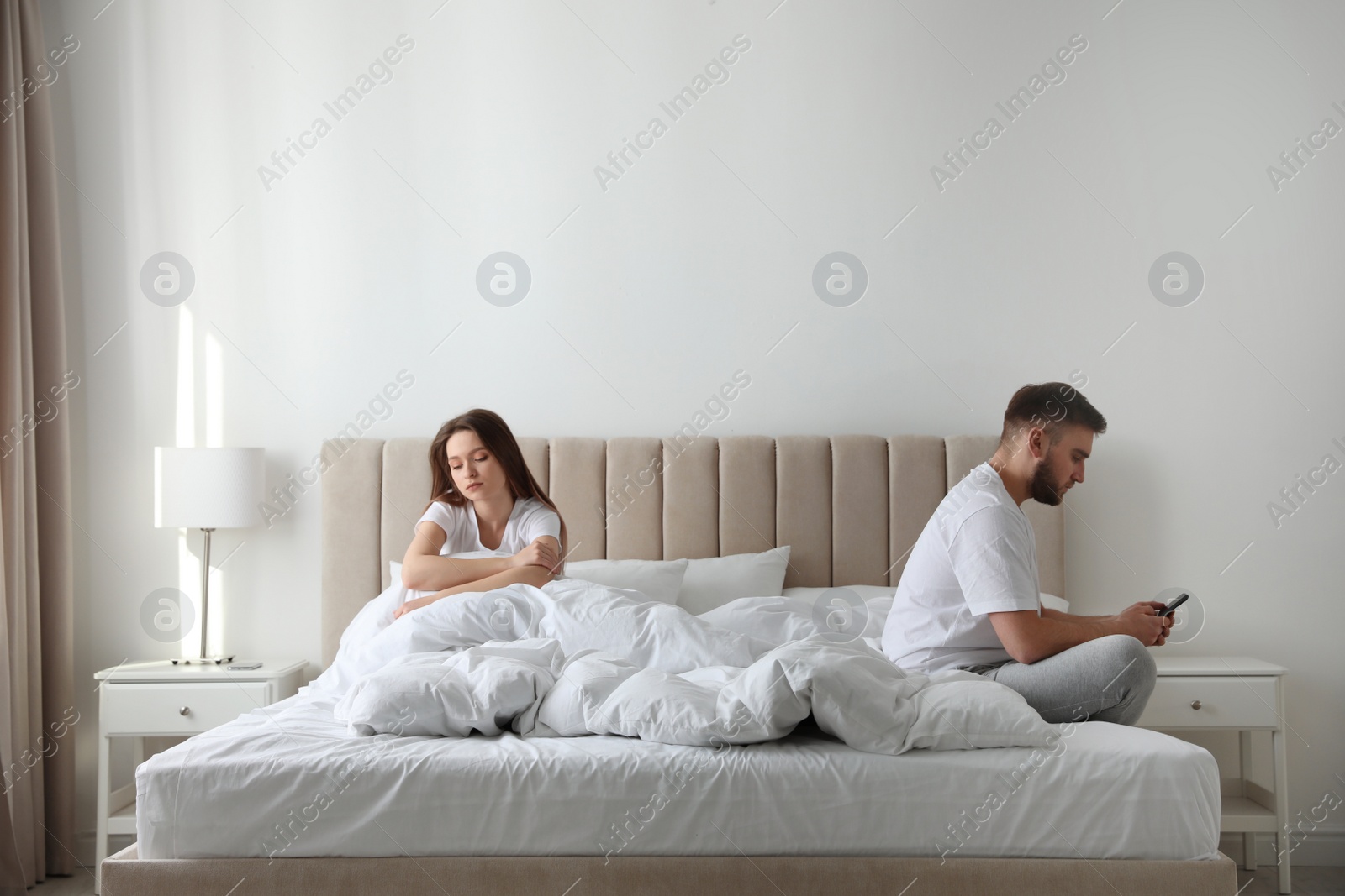 Photo of Young man preferring smartphone over his girlfriend on bed at home. Relationship problems