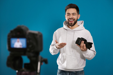 Young blogger with camera recording video against blue background