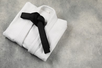 Photo of Black karate belt and white kimono on gray textured background, top view. Space for text