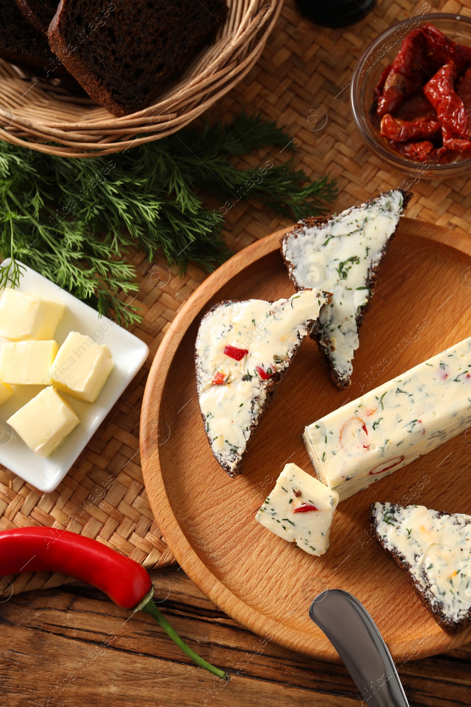 Photo of Tasty butter, dill, chili pepper and rye bread on wooden table, top view