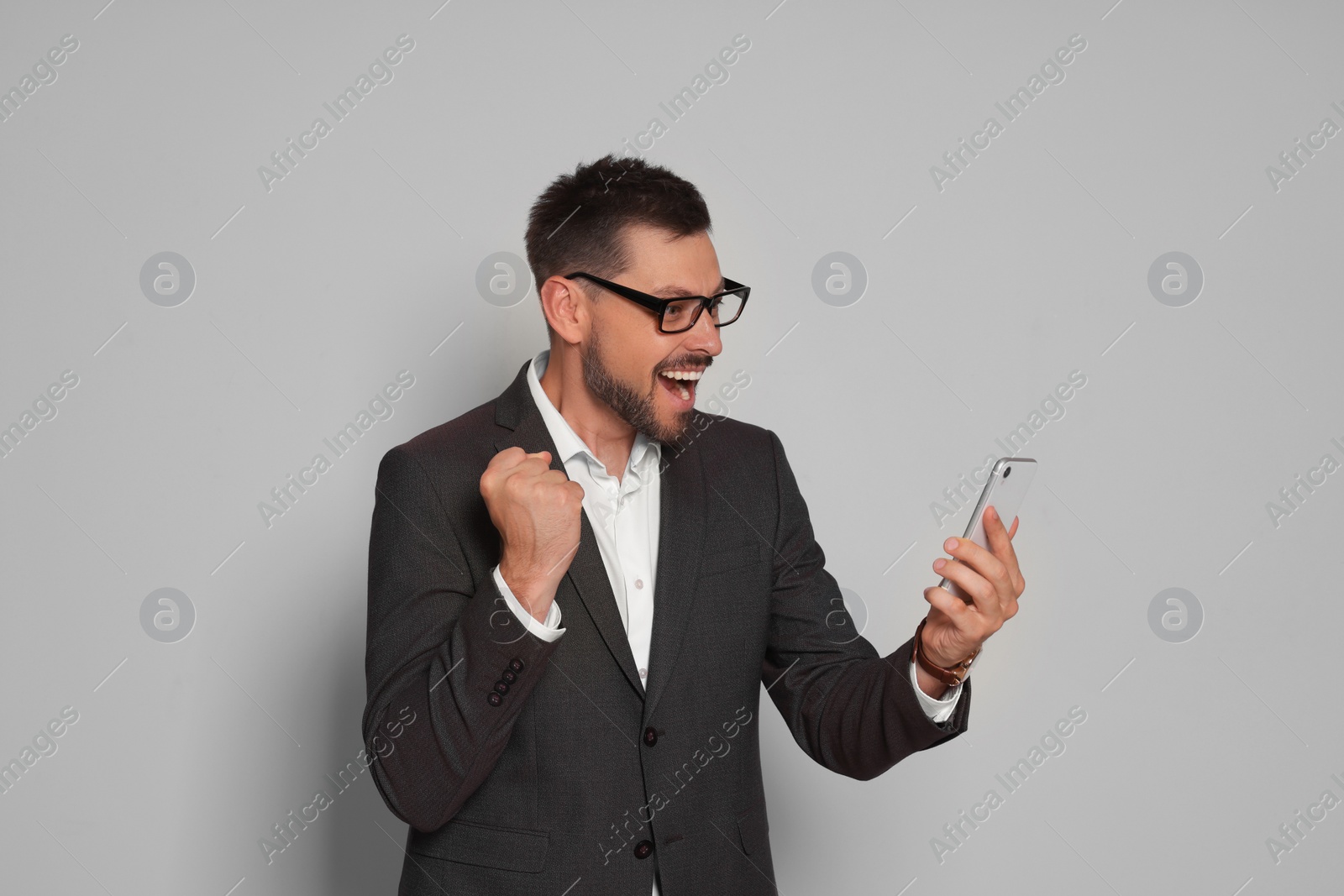 Photo of Emotional man in suit looking at smartphone on light grey background