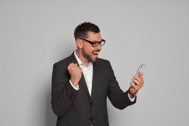 Emotional man in suit looking at smartphone on light grey background