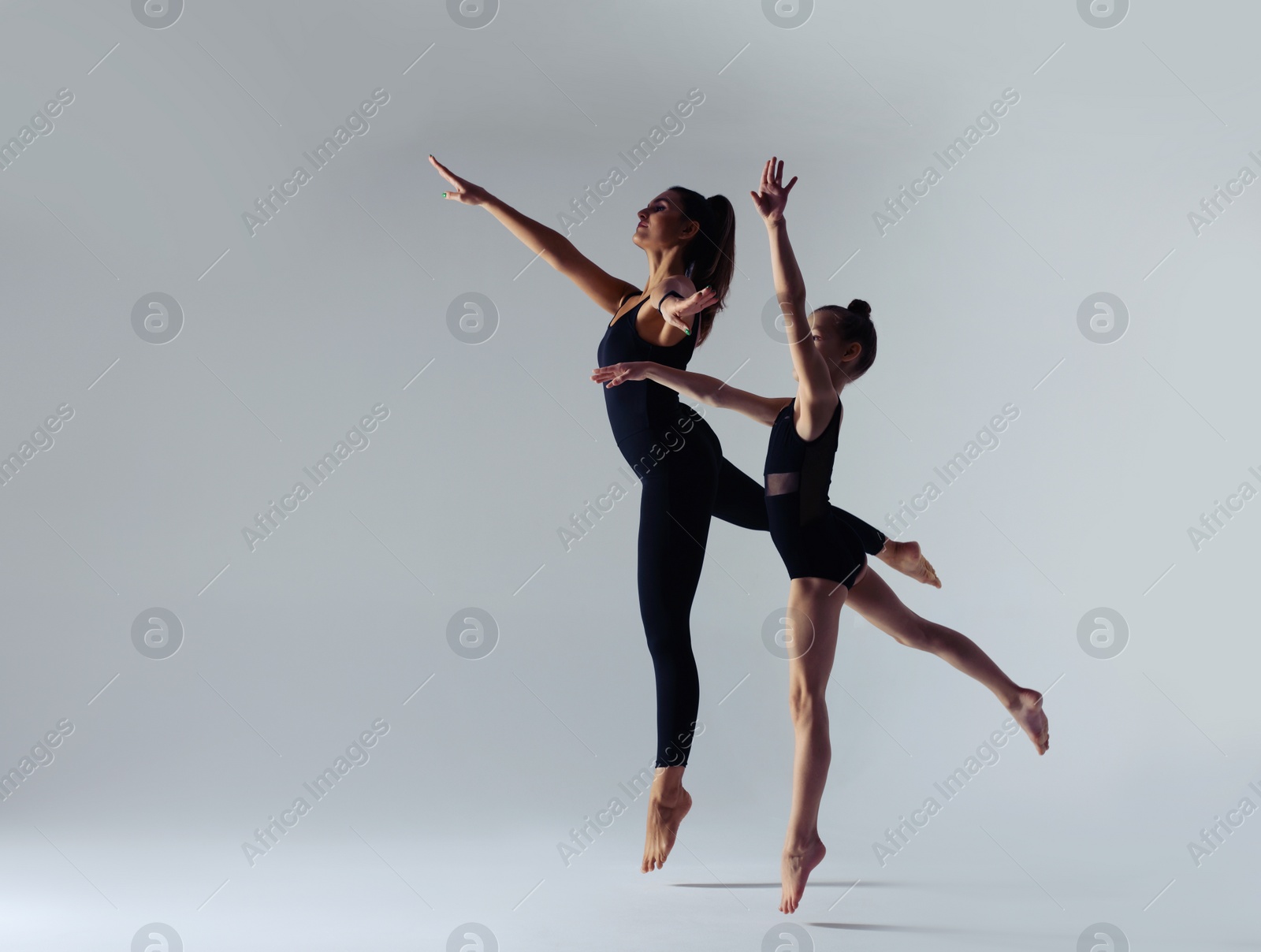 Photo of Little girl and her coach doing gymnastic exercise on white background