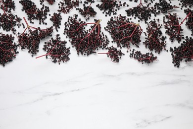 Bunches of ripe elderberries on white marble table, flat lay. Space for text