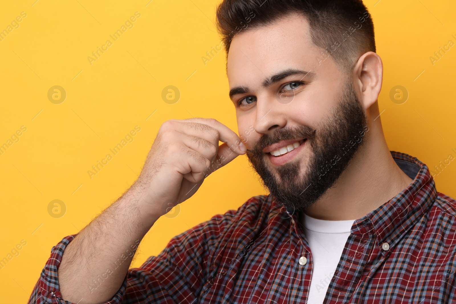 Photo of Happy young man touching mustache on yellow background