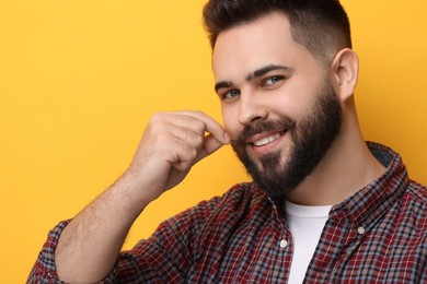 Happy young man touching mustache on yellow background