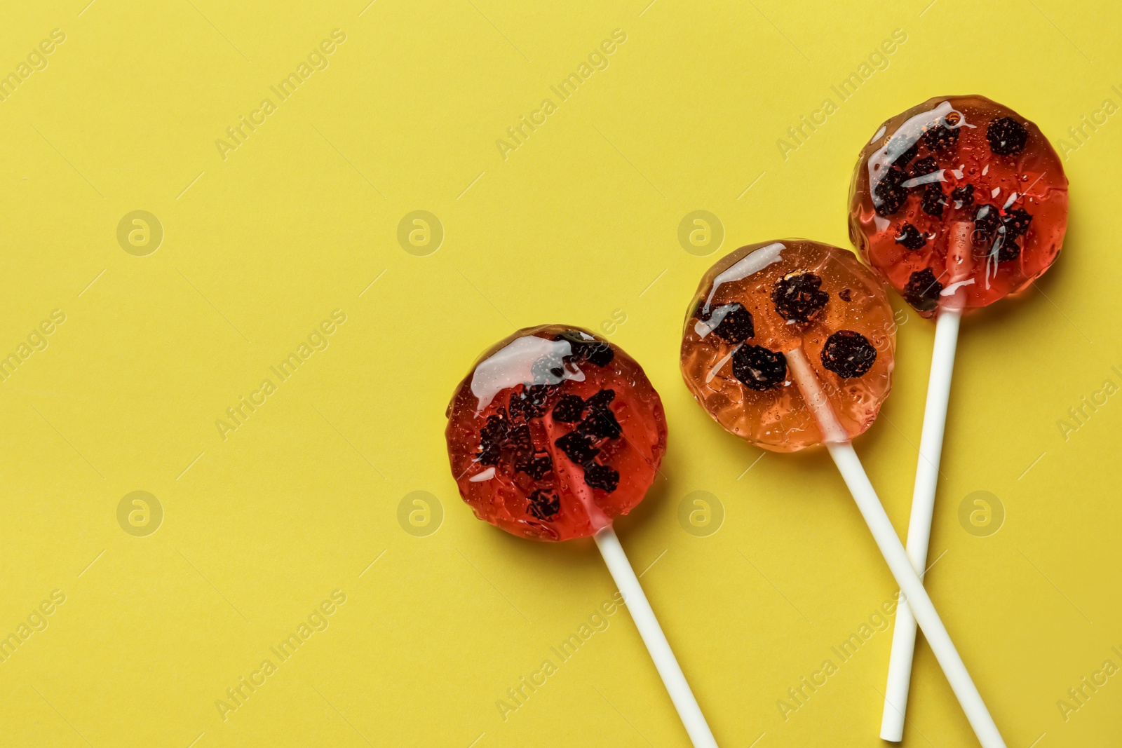 Photo of Sweet colorful lollipops with berries on yellow background, flat lay. Space for text