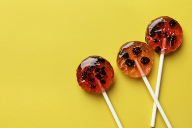 Sweet colorful lollipops with berries on yellow background, flat lay. Space for text