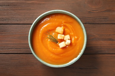Photo of Bowl of tasty sweet potato soup on wooden background, top view