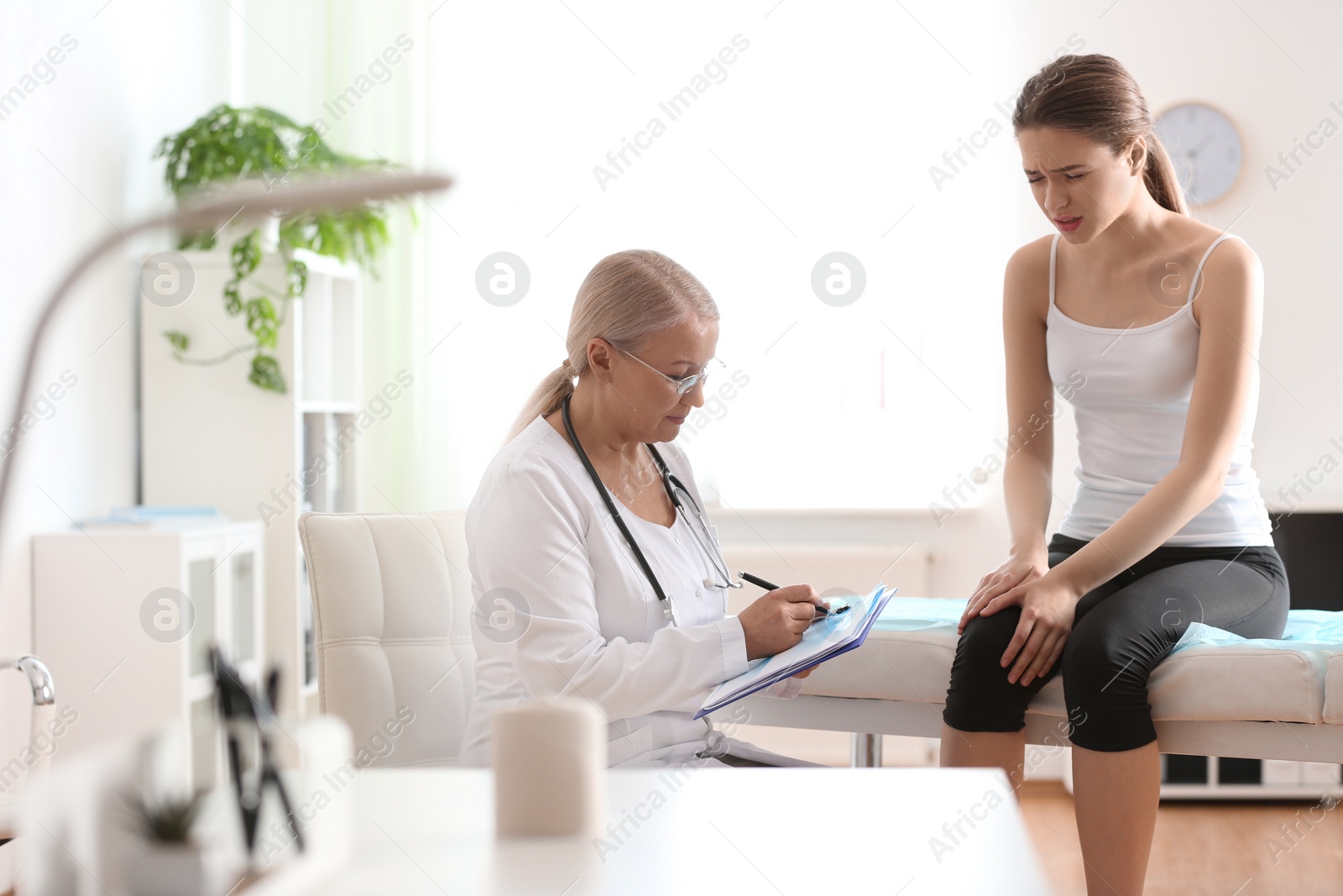 Photo of Female orthopedist examining patient with injured leg in clinic