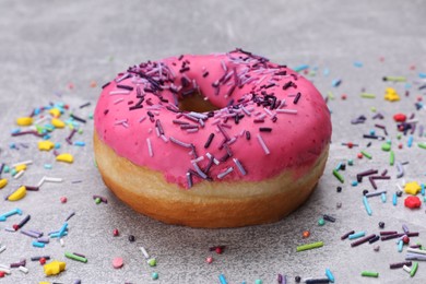 Photo of Sweet glazed donut decorated with sprinkles on light grey table, closeup. Tasty confectionery