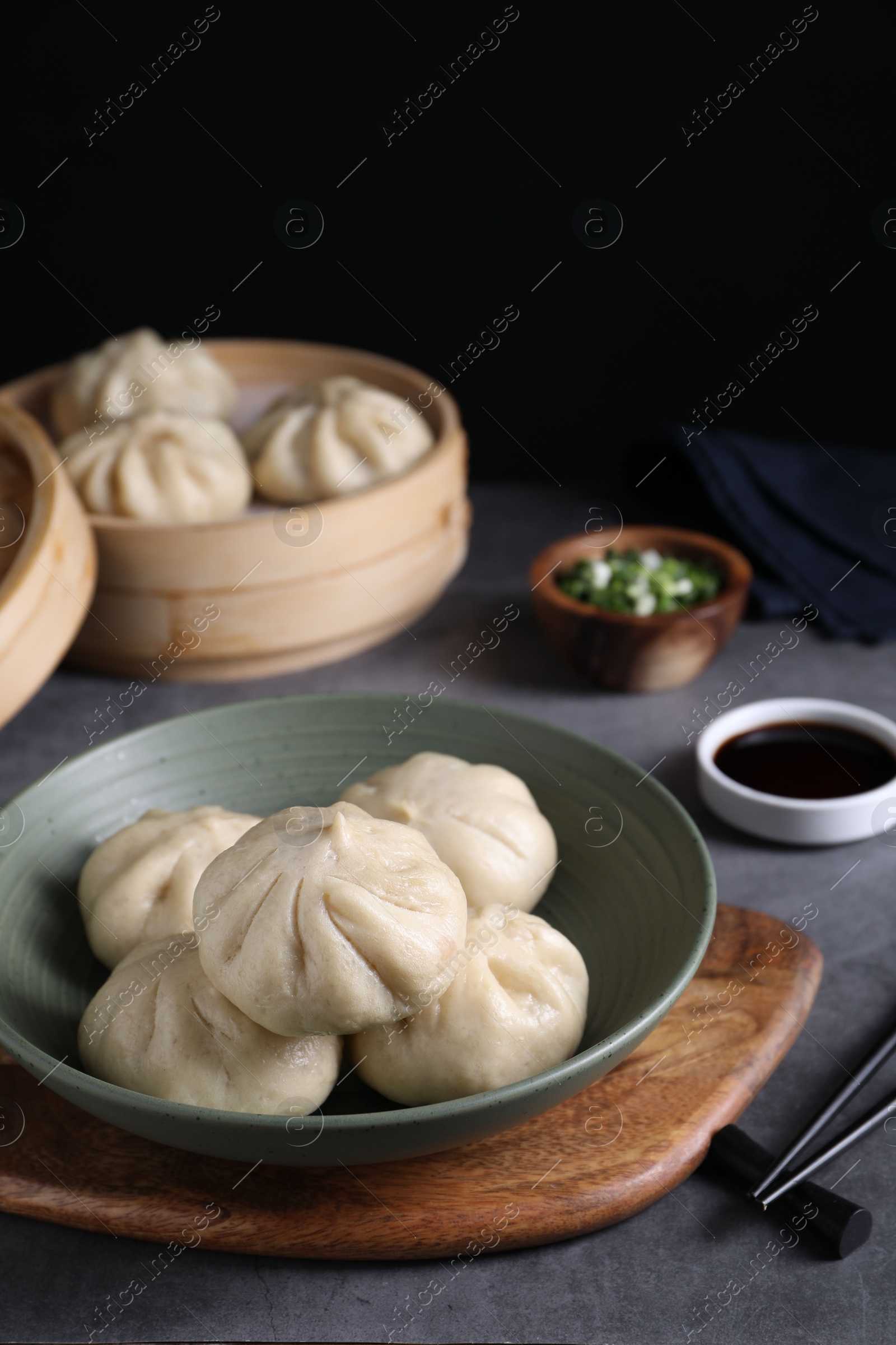 Photo of Delicious bao buns (baozi) in bowl on grey table, closeup