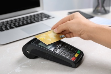 Woman using terminal for contactless payment with credit card at table