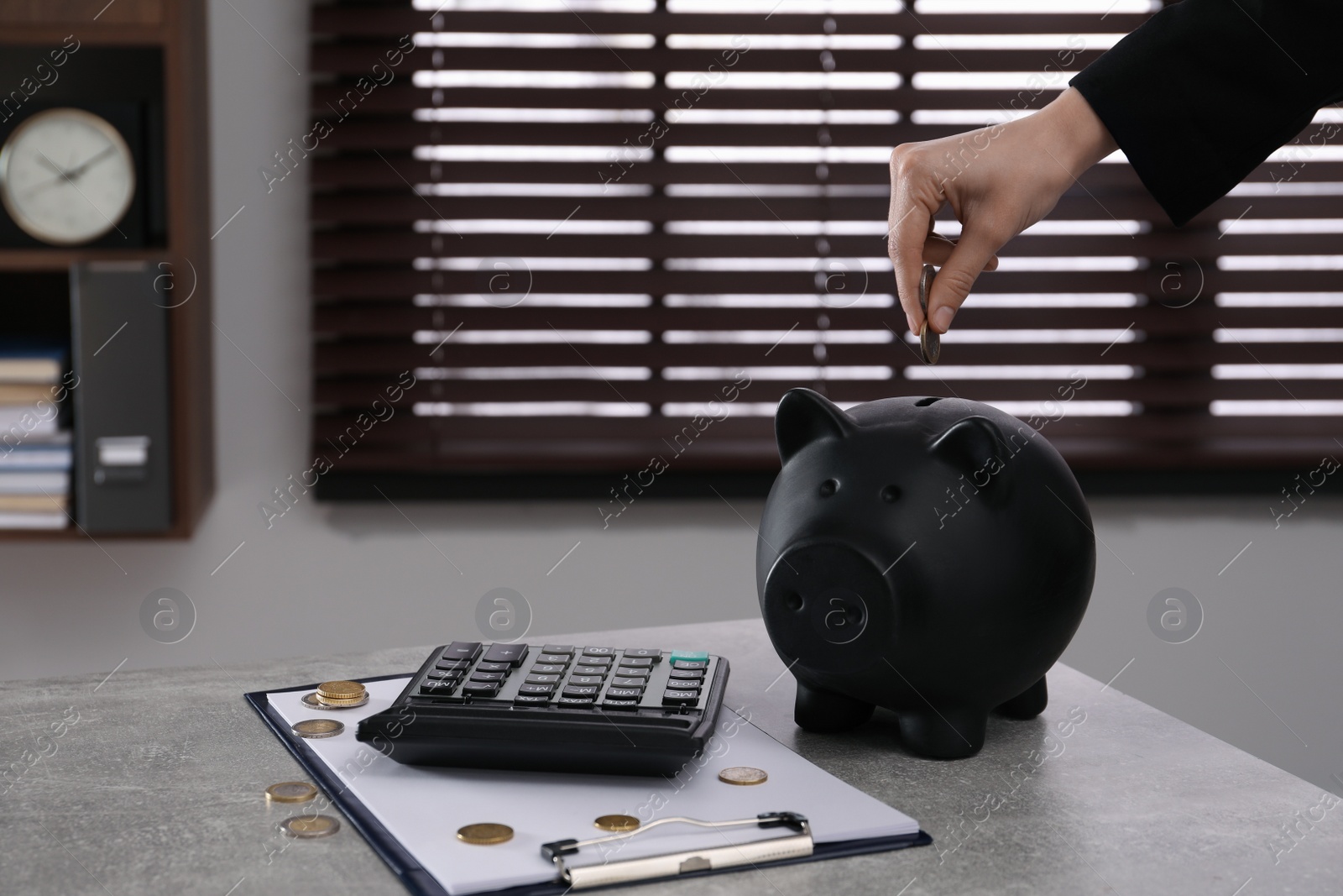 Photo of Woman putting money into piggy bank on grey table in office, closeup
