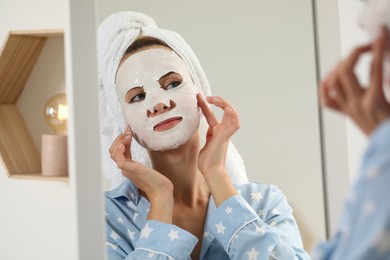 Photo of Young woman with face mask looking into mirror indoors. Spa treatments