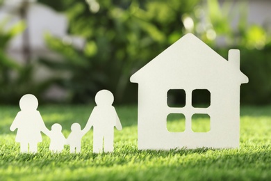 Photo of Paper cutout of family and house on fresh grass. Life insurance concept