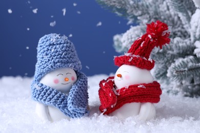Photo of Cute decorative snowmen and fir tree on artificial snow against light blue background, closeup