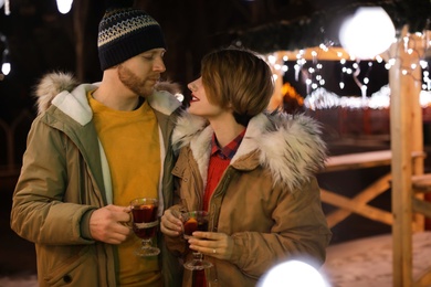 Photo of Young couple with cups of mulled wine at winter fair