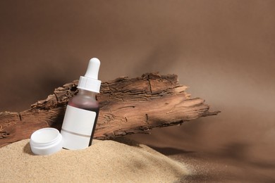 Photo of Cosmetic products and tree bark on sand against brown background. Space for text
