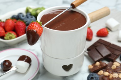 Photo of Fondue pot of melted chocolate and fork with strawberry on white marble table, closeup