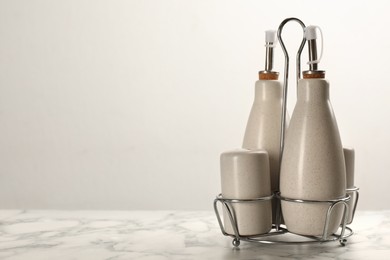 Sauce bottles with salt and pepper shakers in holder on white marble table. Space for text