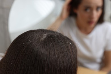 Woman examining her hair and scalp near mirror at home, selective focus. Dandruff problem