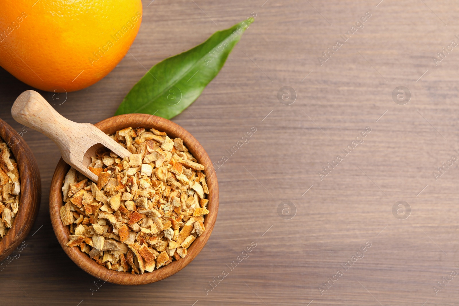 Photo of Bowl of dried orange zest seasoning and fresh fruit on wooden table, flat lay. Space for text