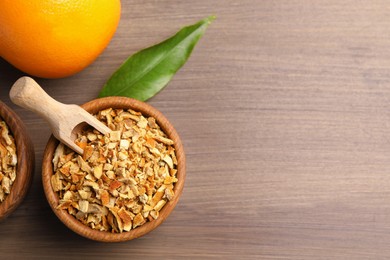 Photo of Bowl of dried orange zest seasoning and fresh fruit on wooden table, flat lay. Space for text