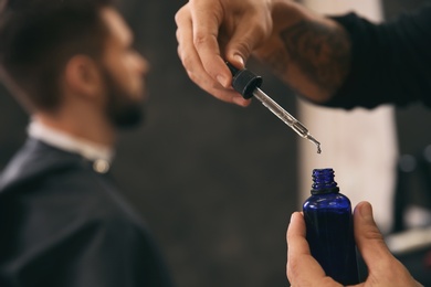 Hairdresser with bottle of beard serum in barbershop. Professional shaving service