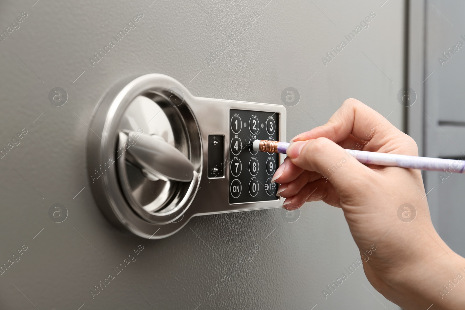 Photo of Woman using pencil to enter code on keypad of modern safe, closeup