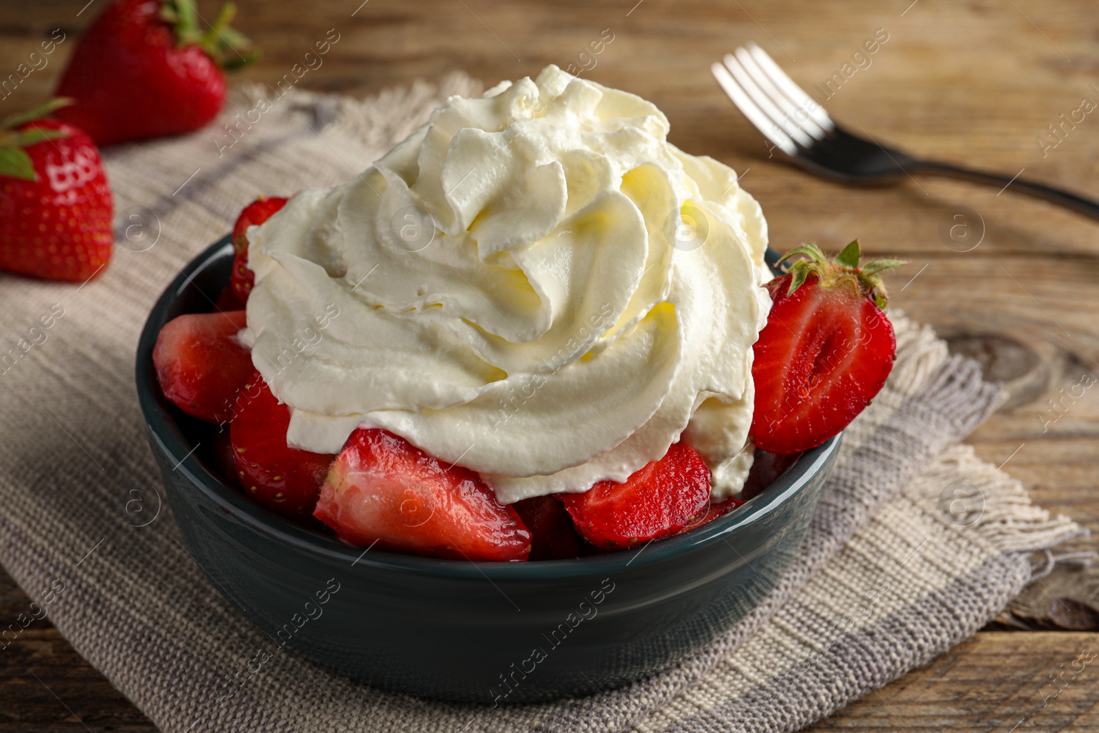 Photo of Bowl with delicious strawberries and whipped cream served on wooden table, closeup