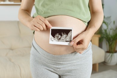 Photo of Pregnant woman with ultrasound picture of baby in living room, closeup