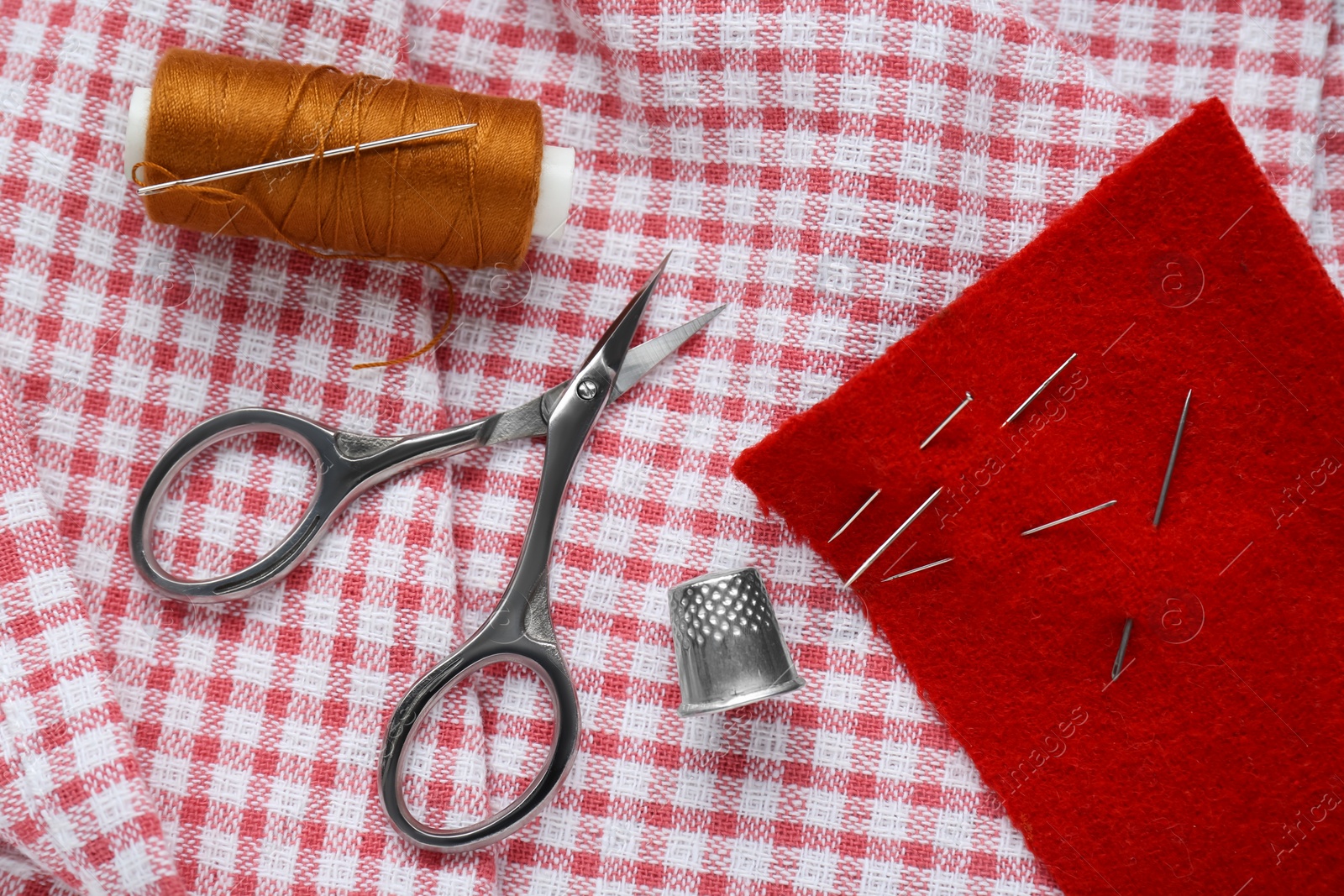Photo of Flat lay composition with thimble and different sewing tools on checkered fabric