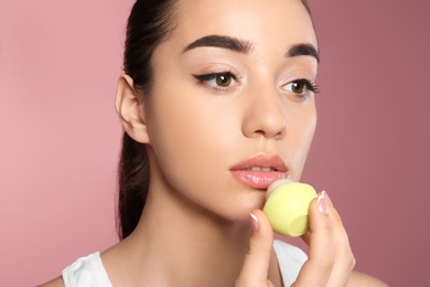 Photo of Young woman applying balm on her lips against color background