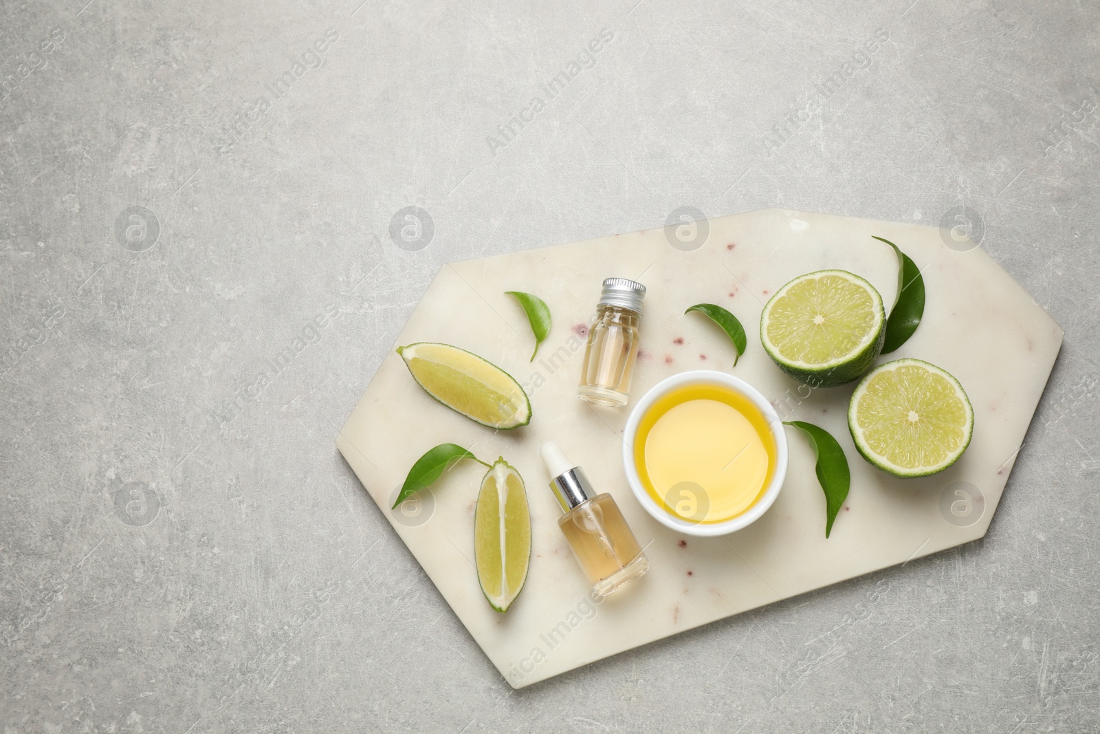 Photo of Lime essential oil and cut citrus fruits on light grey table, top view