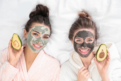 Photo of Young friends with facial masks having fun on bed at pamper party, top view