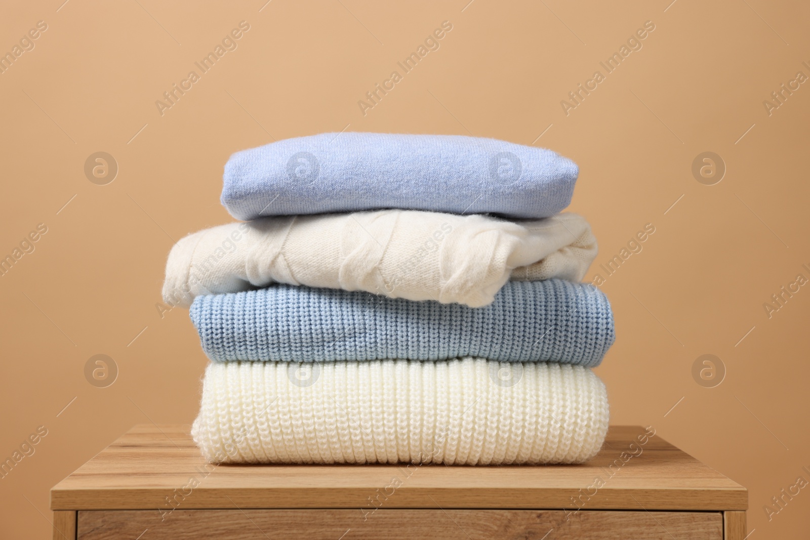 Photo of Stack of casual sweaters on wooden table against light brown background