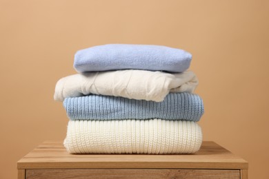 Photo of Stack of casual sweaters on wooden table against light brown background