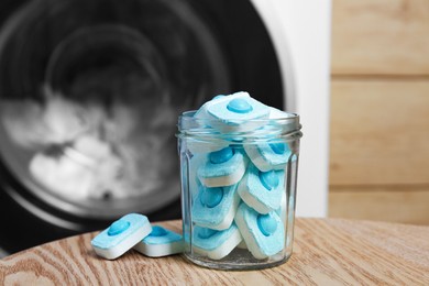 Photo of Jar with water softener tablets on wooden table near washing machine, closeup