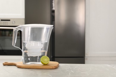 Photo of Water filter jug and lime on light marble table in kitchen, closeup. Space for text