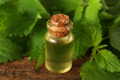 Photo of Glass bottle of nettle oil with leaves on wooden table, closeup