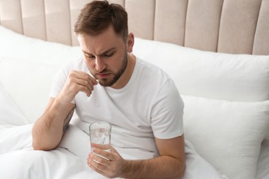 Photo of Man taking pill against migraine in bed