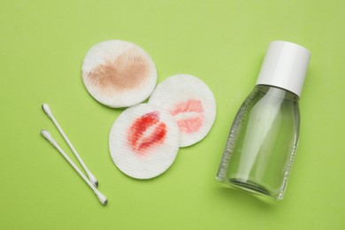 Photo of Dirty cotton pads, swabs and makeup removal product on green background, flat lay