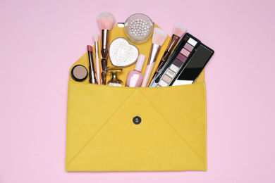 Photo of Cosmetic bag with makeup products on pink background, top view