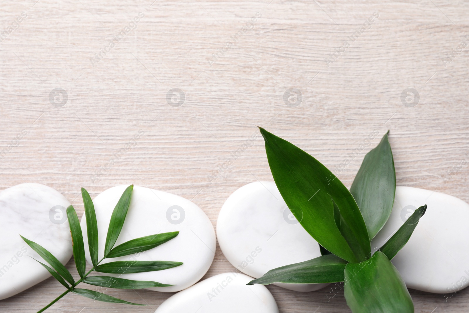 Photo of Spa stones and bamboo leaves on light wooden table, flat lay. Space for text