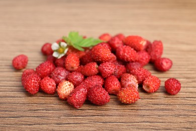 Photo of Pile of wild strawberries, flower and leaves on wooden table, closeup